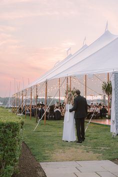 a bride and groom standing under a tent at their outdoor wedding reception in the evening