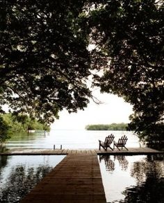 two chairs sitting on top of a wooden dock next to the water's edge