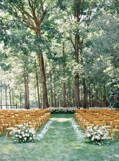 an outdoor ceremony set up with wooden chairs and white flowers on the aisle, surrounded by trees