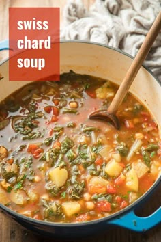 a blue pot filled with vegetable soup on top of a wooden table next to a spoon