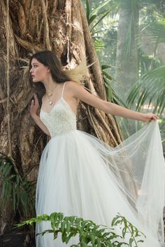 a woman in a white dress standing next to a tree