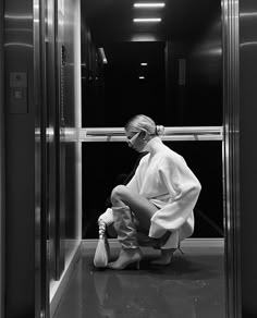 a woman sitting on the ground in front of an elevator door wearing all white clothing