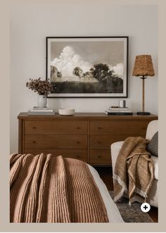 a bed room with a neatly made bed and a painting on the wall above it