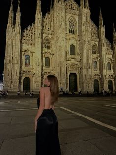 a woman standing in front of a cathedral at night with her back turned to the camera