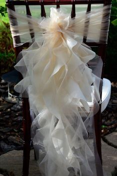 a chair with a white ruffled bow on it's back sitting in front of a tree