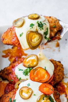 fried chicken with tomatoes, olives and an egg on top is being lifted by a fork