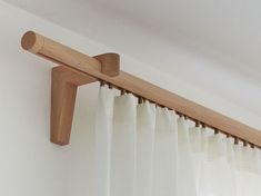 the curtain rod is made from wood and has white drapes on both sides,