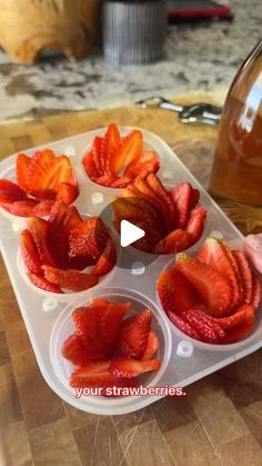 strawberries are placed in muffin cups on a cutting board next to a bottle of honey