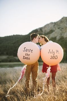 two people holding balloons with the words save the date written on them in front of a mountain