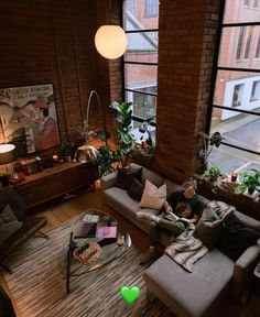 a living room filled with furniture and lots of windows next to a brick wall covered in potted plants