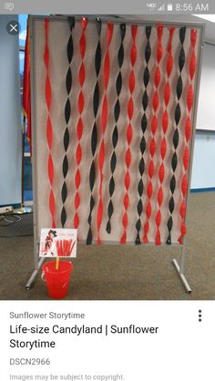 a red bucket is sitting in front of an orange and black wall hanging on a metal frame