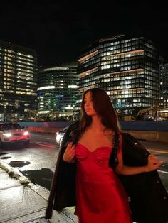 a woman in a red dress is walking down the street at night with her hand on her hip