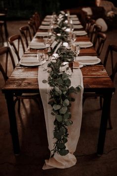 a long table set with place settings and greenery