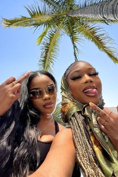 two women standing next to each other under a palm tree with their fingers in the air