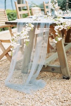 the table is covered with white flowers and sheer fabric, along with a wooden chair