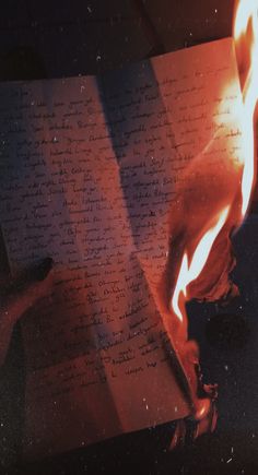 an open book with flames coming out of it on top of a table next to a person's hand