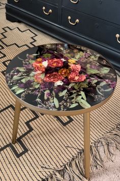 a glass table with flowers on it sitting in front of a dresser and chest of drawers