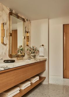 a bathroom with marble counter tops and gold accents on the mirror, along with wooden cabinets