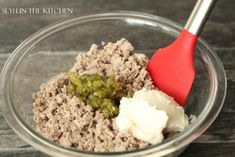 a bowl filled with meat, cream and pickle slices on top of a wooden table