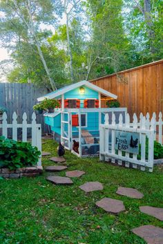 a chicken coop in the back yard with a white picket fence and green grass around it