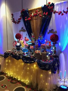 the table is set up for a party with blue and gold decorations, red flowers, and white drapes