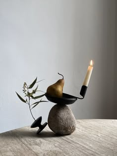 a candle sits on top of a rock with a pear in it and a black bowl