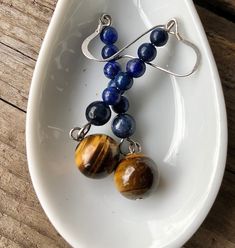 Charming blue Lapis Lazuli and gold Tiger Eye earrings are stunning. These cool 2.25 inch earrings are elegant enough that they would Step up your style game with these stunning earrings, featuring a gorgeous combination of Tiger Eye and Lapis Lazuli. The natural earthy tones of the gemstones make these earrings a versatile accessory that can be dressed up or down, depending on the occasion. With their sophisticated design, these earrings are perfect for a formal setting, but also versatile enou Blue Spiritual Earrings For Gifts, Spiritual Blue Jewelry For Birthday, Spiritual Blue Jewelry For Birthdays, Spiritual Blue Jewelry For Mother's Day, Blue Dangle Earrings For Mother's Day, Blue Jewelry With Matching Earrings For Mother's Day, Blue Dangle Jewelry For Birthday, Blue Dangle Jewelry For Mother's Day, Personalized Blue Dangle Jewelry