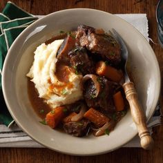 a white plate topped with meat and mashed potatoes next to a wooden serving spoon