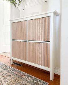 a white cabinet sitting on top of a wooden floor next to a rug and potted plant