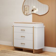 a white dresser sitting next to a mirror on top of a wooden floor in front of a wall