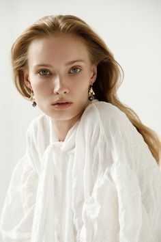 a woman with long blonde hair wearing earrings and a white shirt is looking at the camera