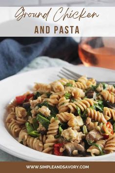 a white plate topped with pasta covered in chicken and veggies next to a glass of wine