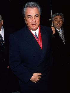 an older man in a suit and tie standing next to other men with umbrellas