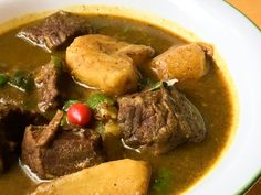 a white bowl filled with stew and potatoes on top of a wooden table next to a spoon