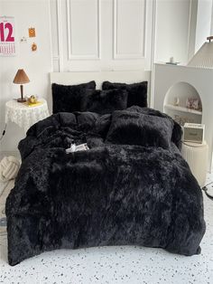 a bed with black comforters and pillows in a white room next to a lamp