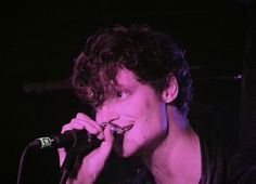 a young man singing into a microphone in front of a purple light on the stage