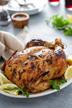 a whole chicken on a plate with lemons and herbs