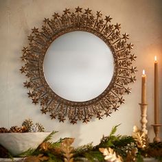 a mirror is hanging on the wall above a mantle with candles and greenery in front of it