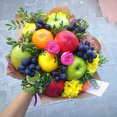 a bouquet of fruit and flowers is being held by someone