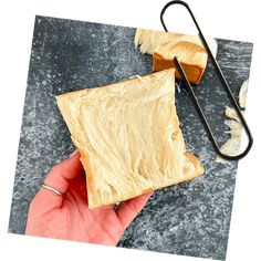 a hand holding a piece of bread next to a pair of tongs