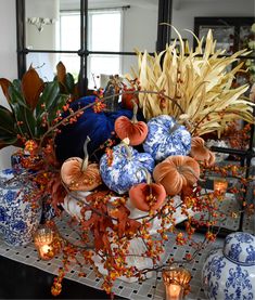 a table topped with blue and white vases filled with pumpkins next to candles