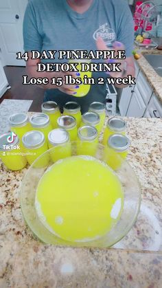 a man sitting in front of a counter filled with yellow drinks and drinking from plastic cups