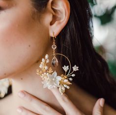 "Our Blyth floral and leaf bridal earrings are so romantic and perfect for the modern bride who wants showstopping wedding jewelry. Available in silver and gold, these gorgeous large hoop earrings feature handscuplted clay flowers, leaves, crystals and pearls.  Wear these earrings with a romantic lace wedding dress, or make them modern with a simple silk gown.  Beautifully accented with plated oak and rose leaves and clustered with a bouquet of hand sculpted clay flowers in various sizes, hand p Gold Flower Cluster Earrings For Wedding, Floral Hoop Earrings For Wedding, Gold Flower Hoop Earrings For Wedding, Gold Floral Hoop Earrings For Wedding, Delicate Flower Hoop Earrings For Weddings, Delicate White Hoop Earrings For Wedding, Flower Hoop Earrings For Wedding, Gold Wedding Earrings With Handmade Flowers, Gold Handmade Flower Earrings For Wedding