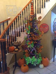 a decorated halloween tree in front of a stair case with pumpkins and other decorations