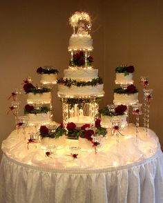 a white wedding cake with red roses and greenery on top is surrounded by wine glasses