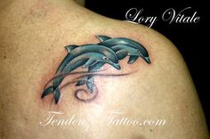 a couple of dolphins on the back of a woman's shoulder and arm tattoo