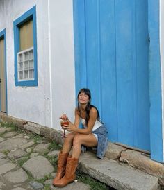 a young woman sitting on the steps in front of a blue and white building with her legs crossed