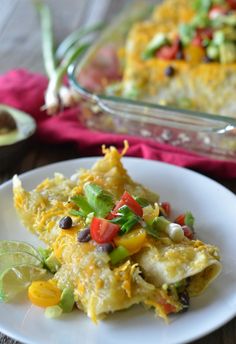 a white plate topped with an enchilada covered in cheese and veggies