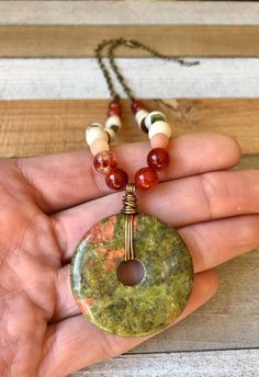 A wire wrapped Unakite donut pendant (2'' x 1.625'') hangs from a bead and bronze plated metal cable chain necklace. Beads include Fire Agate, Rose Aventurine, Vesuvianite & wood beads strung on 0.46 mm flexible wire. This necklace is 18.5'' with a bronze plated metal lobster clasp and 2.125'' bronze plated metal curb chain extender. Nickel and Lead Free. -------------------------------- Healing Properties: Unakite brings together the abundant, nurturing energy of green with the soft, caring Artisan Agate Beaded Round Necklaces, Donut Bead Necklace, Jade Donut Necklace, Donut Gemstone Necklaces, Gemstone Donut Jewelry, Bead Chain Necklace, Donut Pendant, Cardboard Jewelry Boxes, Cable Chain Necklace