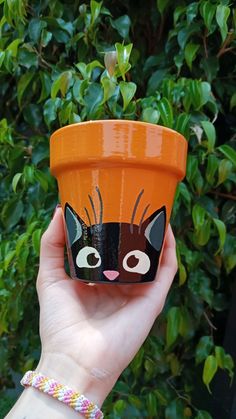 a hand holding an orange cup with a black cat painted on it